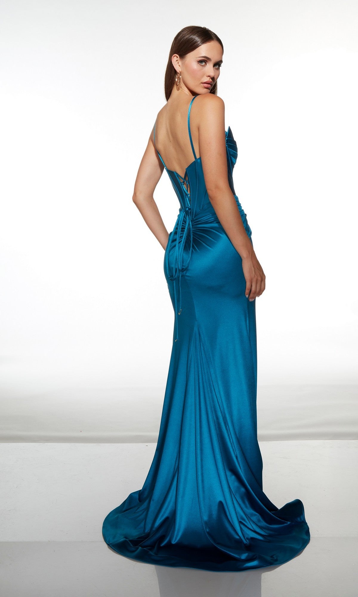 A woman wearing the Alyce 62104 long prom dress in teal satin, featuring thin straps and a lace-up back, stands facing away and looks over her shoulder.